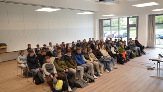 Über 60 Jugendliche nehmen auf Stühlen Platz in einem großen Seminarraum.