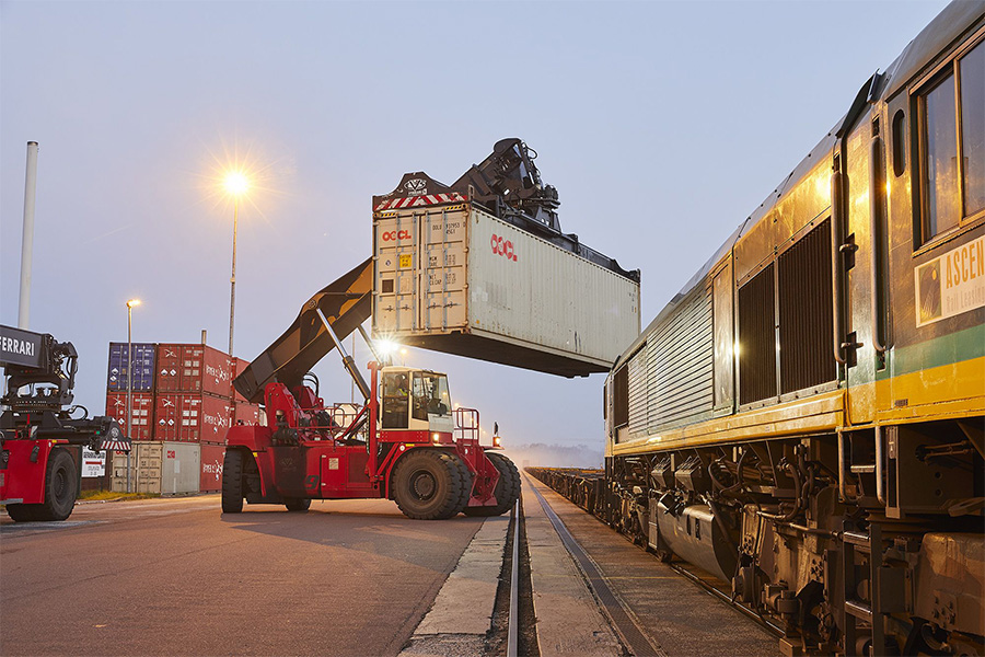 Reachstacker hebt Container auf Bahn.